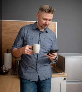 Handsome Man Drinks Coffee In The Kitchen And Watches The News On Phone