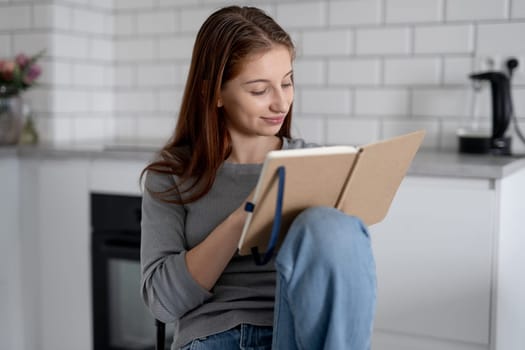 Sweet Teen Girl Reading Notebook Entries While Sitting On A Chair At Home