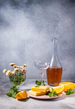 Gourmet orange cheese with mint leaves served with rose wine, orange slices and pink flowers in crystal vases on a grey table