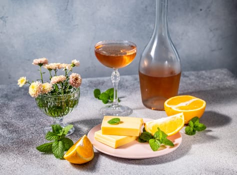 Gourmet setting featuring orange flavored white chocolate bars, a glass and a bottle of wine, orange slices and fresh mint leaves