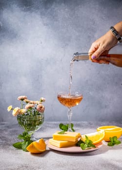 Rose wine being poured into a glass, accompanied by cheese, orange slices, and mint, creating a sophisticated and refreshing scene