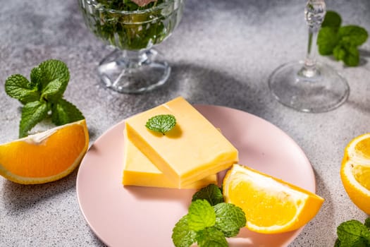 Delicious orange flavored white chocolate pieces garnished with fresh mint leaves, served on a pink plate, creating a refreshing and vibrant dessert