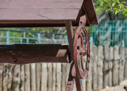 Vintage wooden water well with a hand crank and weathered roof, set against a rustic wooden fence and garden background