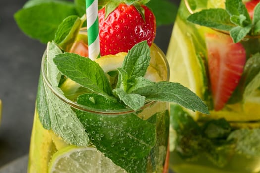 A refreshing drink in a glass with lemon slices, strawberries, fresh mint leaves, and sparkling water, close up