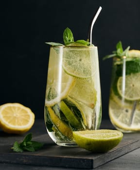 Refreshing detox or summer drink in a glass with lemon, lime, mint, ice, and metal straw. Dark background