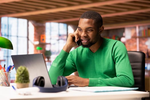 Upbeat man having friendly conversation with friends during telephone call using smartphone. Smiling african american person having fun catching up with mates, talking on phone