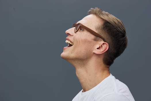 Cheerful smiling man with short brown hair and glasses, looking up and laughing in a bright, clean studio setting. He wears a casual white t-shirt, expressing happiness, positivity, and confidence. Concept: joy of life