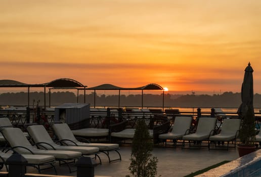 Sun rises over the recliners on deck of Nile cruise boat docked alongside another ship in Edfu Egypt