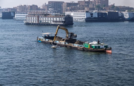 Crowded harbor in Edfu with Nile cruise boats docked and dredging boat removing silt from river