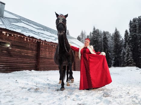 Girl in a colorful national dress stands by a horse in the snowy landscape, celebrating Maslenitsa.