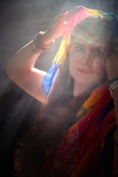 This vibrant photoshoot showcases a middle-aged woman wearing a colorful sari, elegantly posing with a smile and a playful flair.