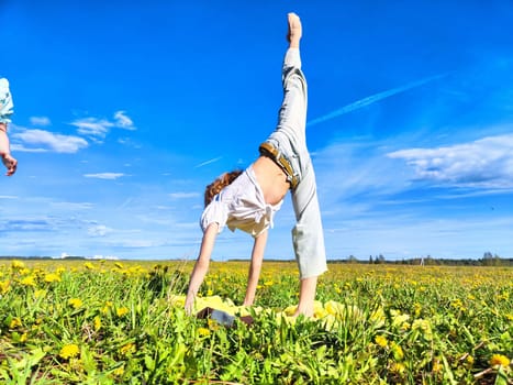A child is performing a handstand in a vibrant meadow surrounded by blooming yellow flowers on a bright sunny day.