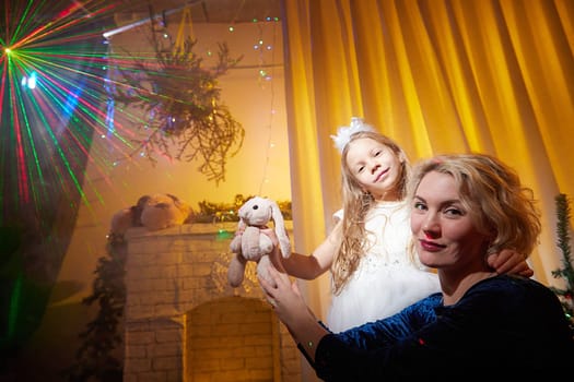 A mother and daughter enjoy the festive atmosphere, holding a stuffed animal while surrounded by holiday lights and decorations.