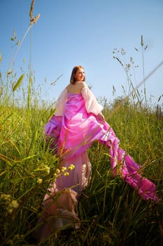 A woman in a vibrant pink gown strolls gracefully through lush green grass under a clear blue sky, embracing the warm sunlight.