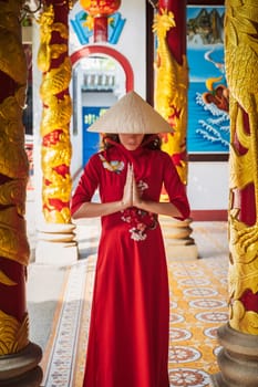 Asian young woman in a traditional Vietnamese hat and costume prays at a temple on a Buddhist pagoda in Vietnam in Asia