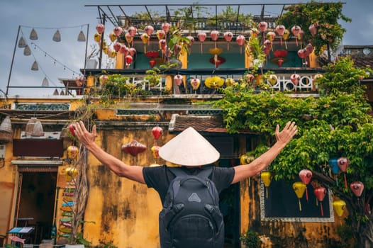 back of an Asian man traveler tourist in traditional vietnamese Non La hat on a street in the old town in Hoi An city in Vietnam in Asia