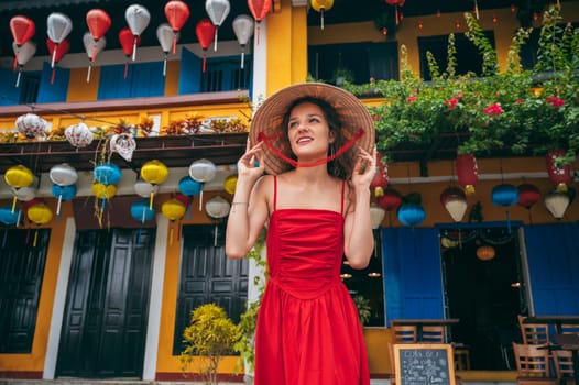 portrait of happy beautiful female tourist in a traditional Vietnamese hat on the street in Hoi An city in Vietnam in Asia