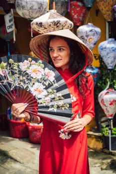 happy beautiful tourist woman in Vietnamese cone hat Non La with a fan in Hoi An in Vietnam in Asia