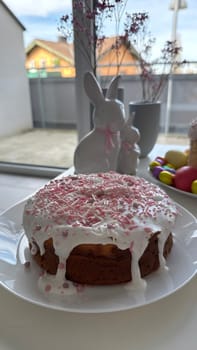Decorated cake with pink icing and colorful sprinkles on a white plate, set against a backdrop of festive decorations, creating a cheerful atmosphere ideal for celebrations and gatherings