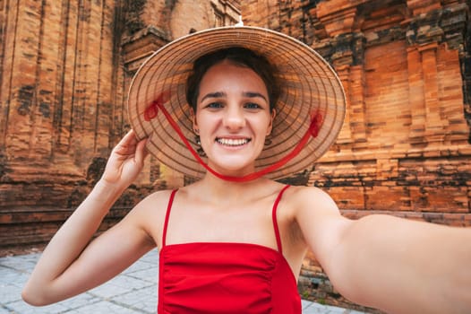 happy young female tourist in a Vietnamese hat takes a selfie at Cham Towers of Po Nagar in Nha Trang in Vietnam in Asia