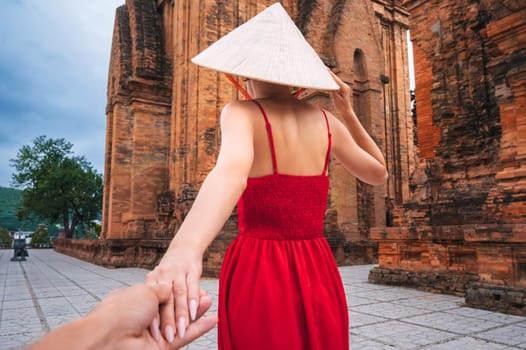Back of a female tourist traveler in a Vietnamese hat Non La at Po Nagar Cham Towers in Nha Trang in Vietnam. The concept of follow me, traveling in Asia