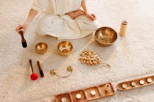 Woman sitting in lotus pose preparing for sound healing session with Tibetan bowls, candles, and ritual tools.