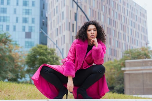 Graceful dancer with curly hair wearing a pink coat, expressing movement and energy in an urban environment. Modern fashion, contemporary dance, and artistic performance against a city backdrop.