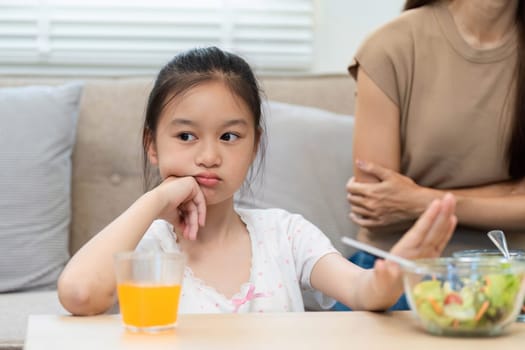 A young girl shows hesitation while her mother encourages her to try healthy salads, focusing on wellness and healthy eating decisions.