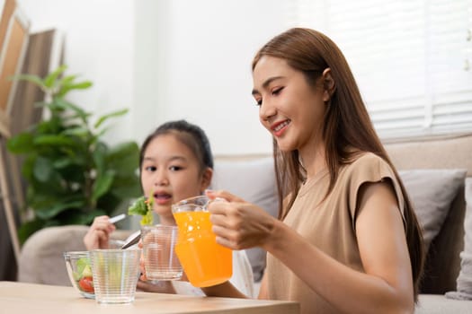A cheerful mother and daughter savoring their nutritious juice and salad, emphasizing wellness and healthy living at home while enjoying family time.
