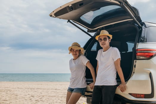Asian couple is posing in back of a car enjoying beautiful views on the ocean beach. lifestyle man and the woman is wearing hat. Scene is relaxed and carefree, love and travel summer trip concept