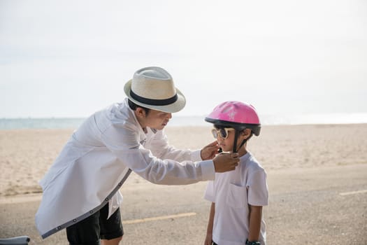 Family travel concept, A father wearing a safety helmet engages in an inspiring lesson teaching his cheerful son the joy and freedom of riding a bicycle on the beach a memorable tourism day.