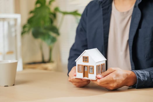 Close-up of a real estate agent hand holding a small house model, symbolizing property, home loan, and finance concepts. Represents the role of an agent in real estate, housing, and loan planning.
