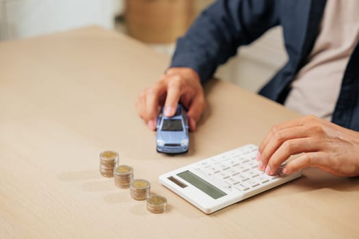 A person uses a calculator near coins and a car model, calculating auto loan payments and taxes. Perfect for car sales, finance, insurance, and banking concepts in financial planning.