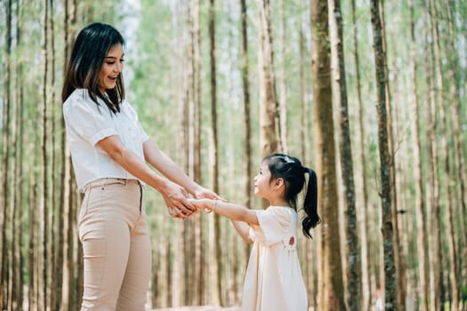 Asian mother and daughter walking hand in hand through a forest, Happy mother and little child holding hands together, Family day
