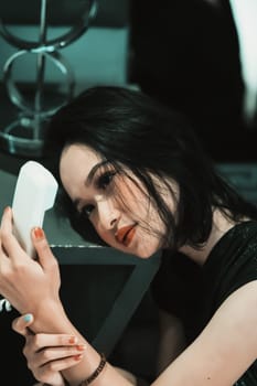 Asian Woman staring and holding the white phone in her hand while wearing a black dress and bracelet in her hand in the bedroom
