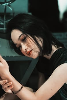 Asian Woman staring and holding the white phone in her hand while wearing a black dress and bracelet in her hand in the bedroom