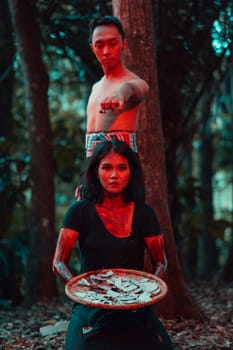 a couple of serial killers have bodies covered in blood and are performing a satanic ritual in the middle of a forest before sunset