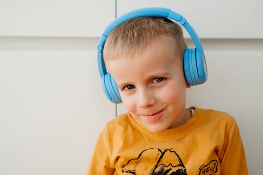 portrait of a 4-year-old boy in an orange sweatshirt and blue headphones listening to music. High quality photo