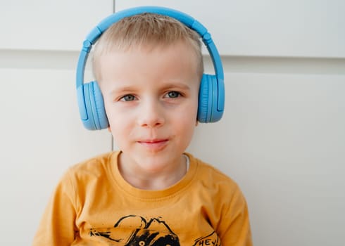 portrait of a 4-year-old boy in an orange sweatshirt and blue headphones listening to music. High quality photo