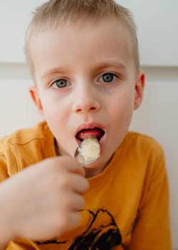 a 4-year-old blond boy eats honey from a spoon with his mouth open.. High quality photo
