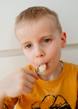 a 4-year-old blond boy eats honey from a spoon with his mouth open. High quality photo