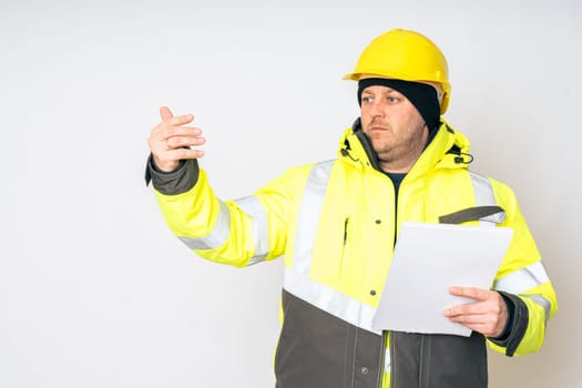 a man in a yellow working winter jacket, yellow safety helmet with papers in his hands. High quality photo