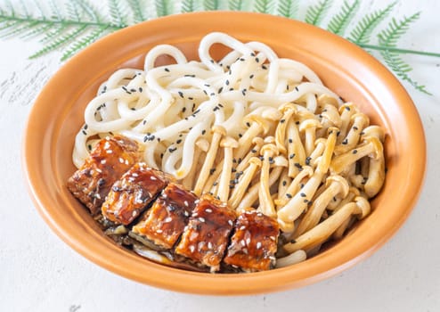 A hearty udon bowl topped with eel, mushrooms, and toasted sesame garnish