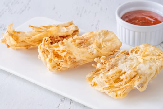 Golden enoki clusters deep-fried to crunch perfection beside sweet chili dipping bowl