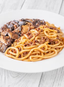 White plate of thick udon with beef, and mushroom topping