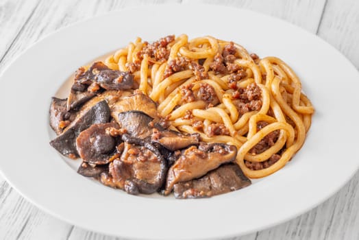White plate of thick udon with beef, and mushroom topping