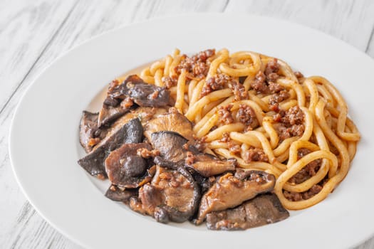 White plate of thick udon with beef, and mushroom topping