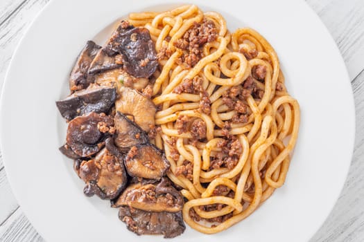 White plate of thick udon with beef, and mushroom topping