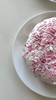 Round cake adorned with pink sprinkles and creamy icing on a white plate, presenting a delightful dessert ideal for celebrations and special occasions, a sweet treat that brings joy