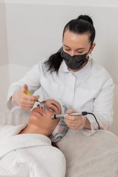 Caucasian woman girl receives non-invasive face rejuvenation during electroporation procedure. Cosmetologist applies advanced therapy in beauty clinic to improve skin tone and reduce signs of aging.